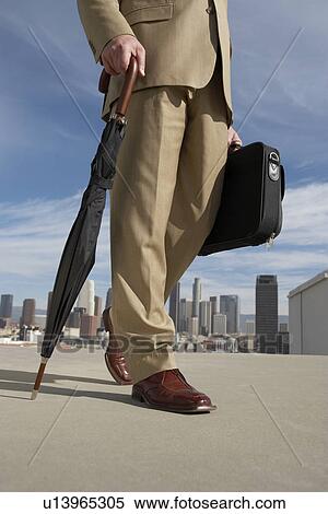 Stock Photography - Man walking with umbrella and briefcase on city street low section. Fotosearch