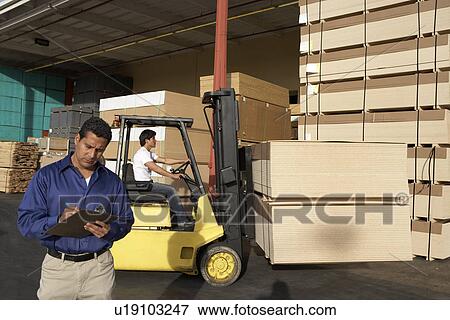 Man with clipboard in front of forklift stacking boxes View Large Photo Image Stock Photo - Man with clipboard in front of forklift stacking boxes. Fotosearch