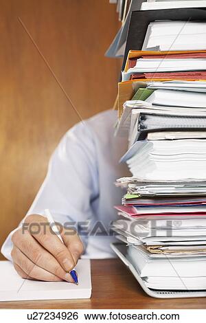 Man writing close-up of arm and hand sitting behind stack of paperwork at desk View Large Photo Image Stock Photograph - Man writing close-up of arm and hand sitting behind stack of paperwork at desk. Fotosearch