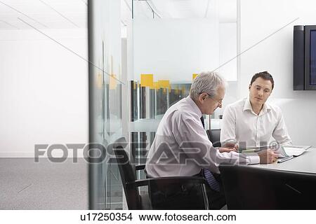 Picture - Mature businessman and office worker sitting at conference table. Fotosearch