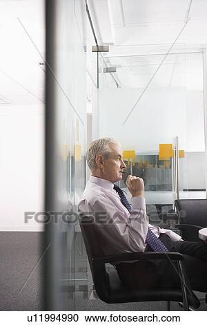 Stock Image - Mature businessman sitting in conference room side view. Fotosearch