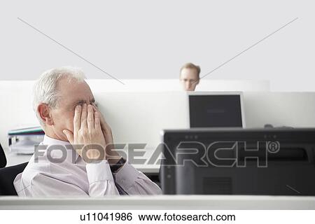 Mature businessman sitting rubbing eyes in office cubicle View Large Photo Image Stock Photograph - Mature businessman sitting rubbing eyes in office cubicle. Fotosearch