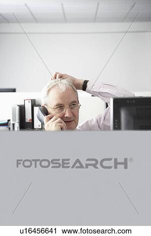 Mature businessman using telephone with hand on head in office cubicle View Large Photo Image Stock Image - Mature businessman using telephone with hand on head in office cubicle. Fotosearch