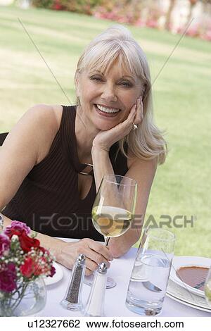 Stock Image - Mature elegant woman sitting at table outdoors. Fotosearch