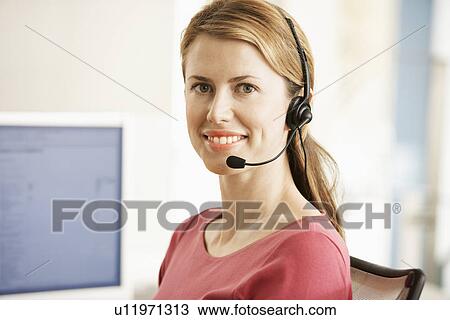 Stock Image - Mid-adult female office worker sitting in cubicle wearing headset portrait. Fotosearch