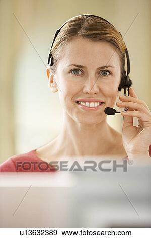 Stock Photo - Mid-adult female office worker sitting in cubicle wearing headset portrait. Fotosearch