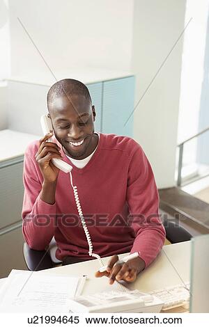 Mid-adult male office worker at desk talking on phone View Large Photo Image Stock Photography - Mid-adult male office worker at desk talking on phone. Fotosearch