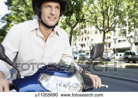 Mid-adult man riding motorscooter along city street View Large Photo Image Stock Image - Mid-adult man riding motorscooter along city street. Fotosearch