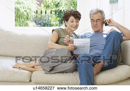 Stock Photo - Middle-aged couple paying bill by phone. Fotosearch