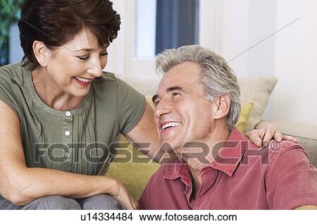 Picture - Middle-aged couple sitting smiling looking into eyes. Fotosearch