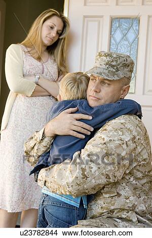 Military father embracing son (5-6) outside home wife watching View Large Photo Image Picture - Military father embracing son (5-6) outside home wife watching. Fotosearch