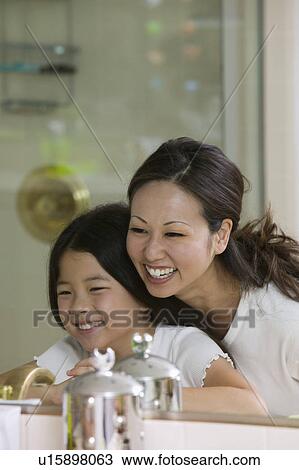 Stock Image - Mother and Daughter Looking at reflection in Bathroom mirror focus on mirror. Fotosearch