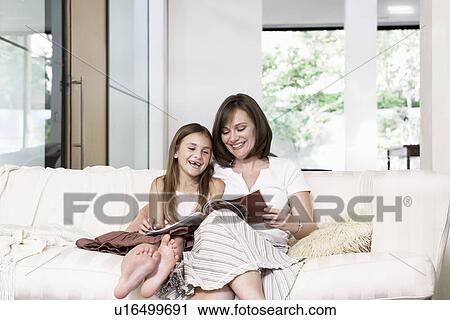 Stock Image - Mother and daughter reading book in living room portrait. Fotosearch