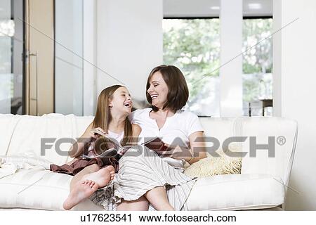 Stock Image - Mother and daughter reading book in living room portrait. Fotosearch