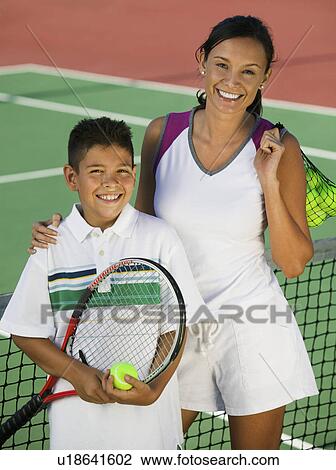 Stock Image - Mother and son by net on tennis court portrait high angle view. Fotosearch