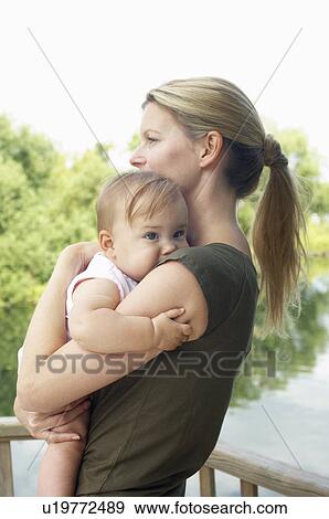 Mother holding daughter by lake half length View Large Photo Image Stock Photo - Mother holding daughter by lake half length. Fotosearch