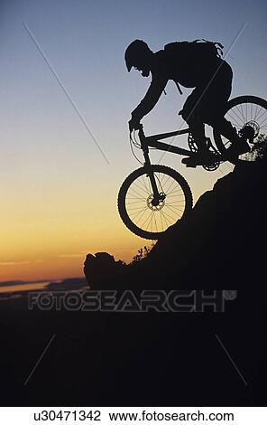 Stock Image - Mountain biker riding down slope. Fotosearch
