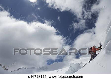 Stock Image - Mountain climber going up snowy slope with axes. Fotosearch