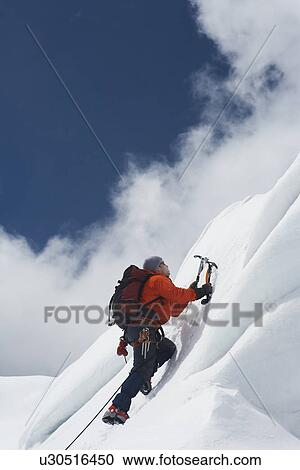 Stock Image - Mountain climber going up snowy slope with axes. Fotosearch