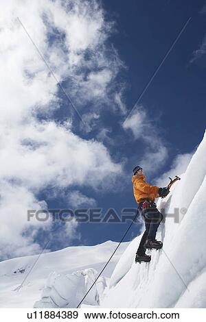 Stock Photo - Mountain climber going up snowy slope with axes. Fotosearch