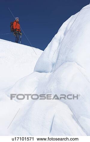Stock Image - Mountain climber hiking past ice formation. Fotosearch