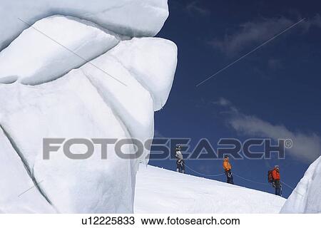 Stock Image - Mountain climbers hiking past ice formation. Fotosearch