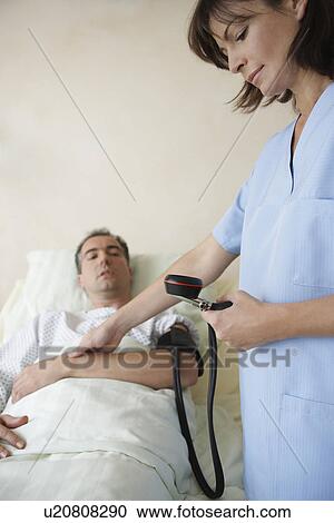 Stock Image - Nurse Taking blood pressure and pulse of patient in hospital bed. Fotosearch