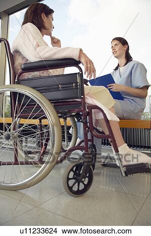 Picture - Nurse talking to patient in wheelchair low angle view. Fotosearch
