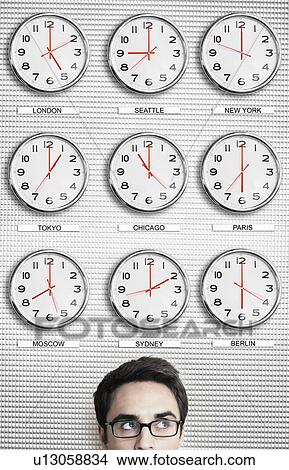 Picture - Office worker in front of clocks showing time across the world. Fotosearch