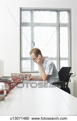 Office worker sitting using mobile phone at desk with document trays side view View Large Photo Image Stock Image - Office worker sitting using mobile phone at desk with document trays side view. Fotosearch