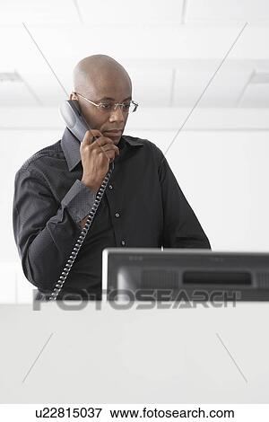 Office worker standing in office using telephone View Large Photo Image Stock Photo - Office worker standing in office using telephone. Fotosearch