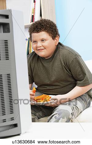 Overweight Boy (13-15) Eating Carrot Sticks in Front of Television View Large Photo Image Picture - Overweight Boy (13-15) Eating Carrot Sticks in Front of Television. Fotosearch