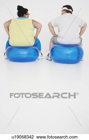 Stock Image - Overweight man and woman Resting on Exercise Balls back view. Fotosearch
