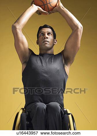 Stock Photo - Paraplegic athlete sitting in wheelchair shooting basketball. Fotosearch