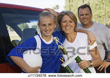 Stock Photo - Parents with daughter (13-17) holding soccer trophy portrait. Fotosearch