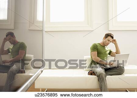 Pensive man using laptop on modern sofa in modern apartment View Large Photo Image Stock Photography - Pensive man using laptop on modern sofa in modern apartment. Fotosearch