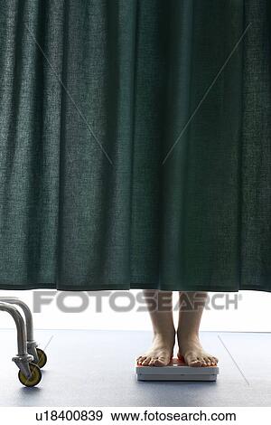 Stock Photo - Person on weighing scales behind curtain in hospital low section. Fotosearch