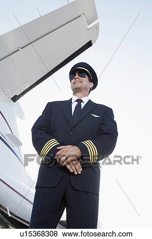 Stock Photo - Pilot in uniform standing Beside an Airplane hands clasped low angle view. Fotosearch