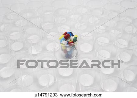 Stock Image - Plastic cup containing pills surrounded by empty glasses. Fotosearch