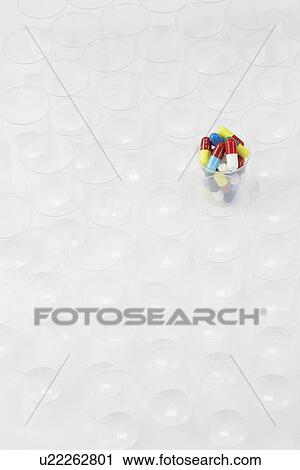 Stock Image - Plastic cup containing pills surrounded by empty glasses. Fotosearch