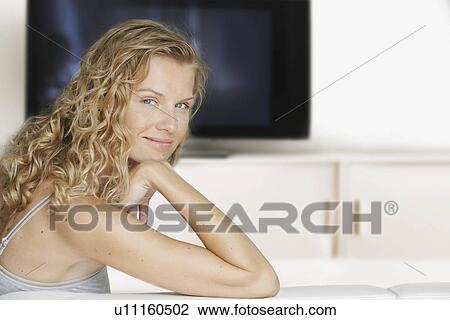 Stock Image - Portrait of woman sitting on sofa side view. Fotosearch