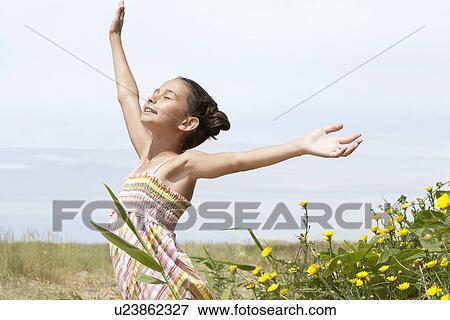 Pre-teen girl standing beside flowers eyes closed arms outstretched side view View Large Photo Image Stock Photo - Pre-teen girl standing beside flowers eyes closed arms outstretched side view. Fotosearch