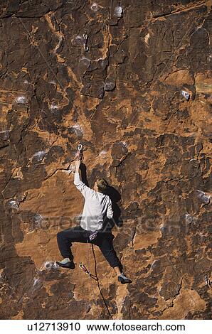 Stock Image - Rock climber climbing cliff. Fotosearch