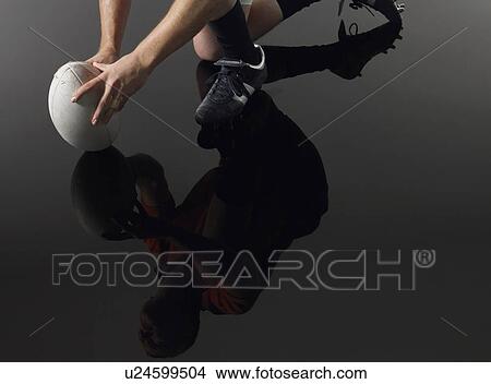 Rugby player kneeling on one knee holding ball low section with reflection elevated view View Large Photo Image Picture - Rugby player kneeling on one knee holding ball low section with reflection elevated view. Fotosearch