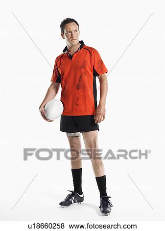 Stock Photo - Rugby player standing holding ball. Fotosearch