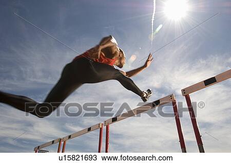 Runner jumping over running hurdle low angle view View Large Photo Image Stock Image - Runner jumping over running hurdle low angle view. Fotosearch