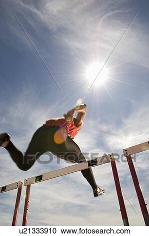 Stock Image - Runner jumping over running hurdle low angle view. Fotosearch