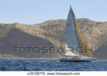 Stock Image - Sailboat by coastline on ocean. Fotosearch