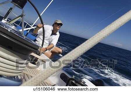 Stock Photograph - Sailor at helm of yacht on ocean. Fotosearch