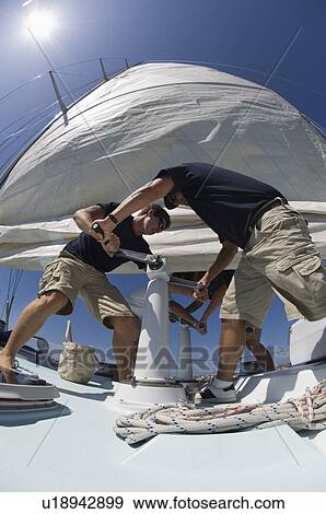 Stock Photo - Sailors operating windlass on yacht low angle view wide angle lens. Fotosearch